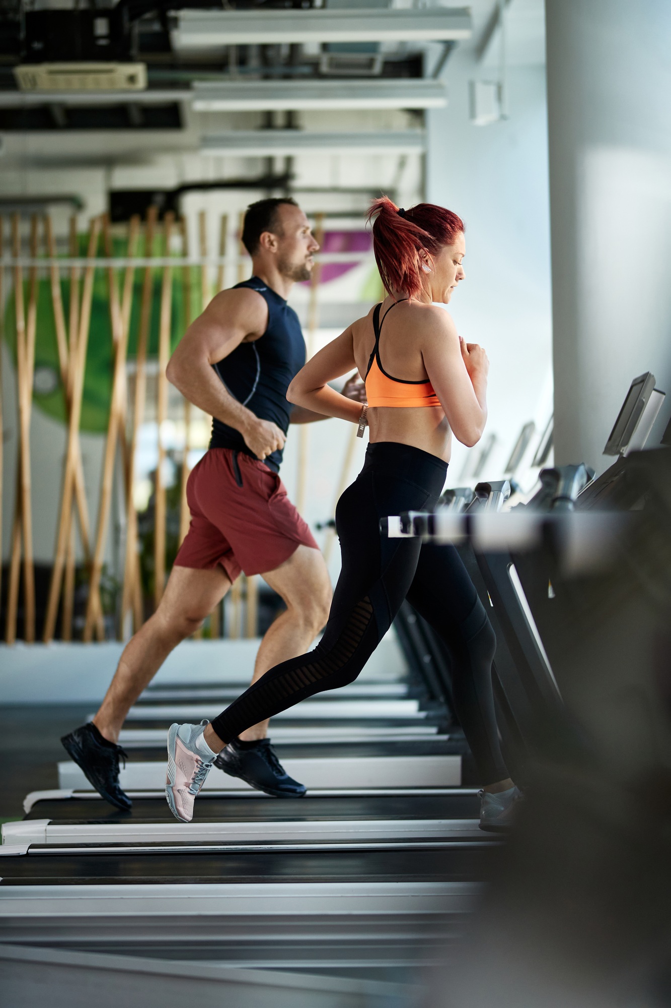 Athletic couple jogging on treadmills during sports training in a gym.